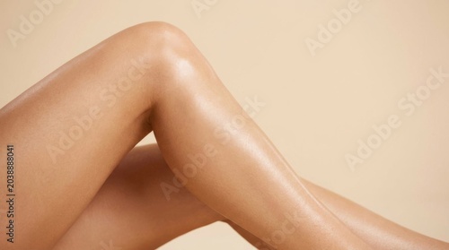 Close up of smooth and tanned female legs with glowing skin on beige background.