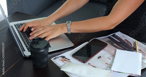 Hands typing on laptop beside coffee, phone and envelopes, closeup captures small business owner processing orders and customer messages with focused steady keystrokes in busy workspace.