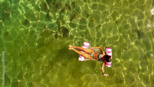 Canvastavla Breathtaking aerial view of a young woman relaxing on a colorful inflatable matt