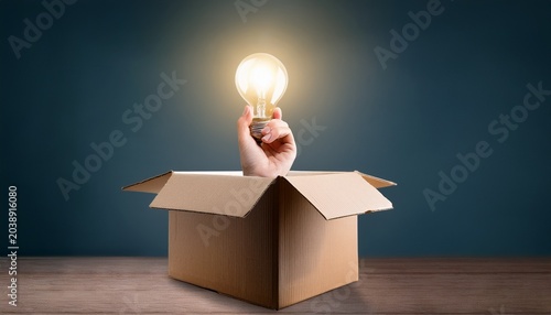 hand coming out of a cardboard box holding a light bulb concept of idea and creativity