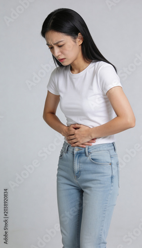 Young asian woman suffering from severe abdominal pain while holding stomach. Symptom of digestive disorder, stomachache or menstruation. Healthcare vertical concept, medical condition, discomfort.