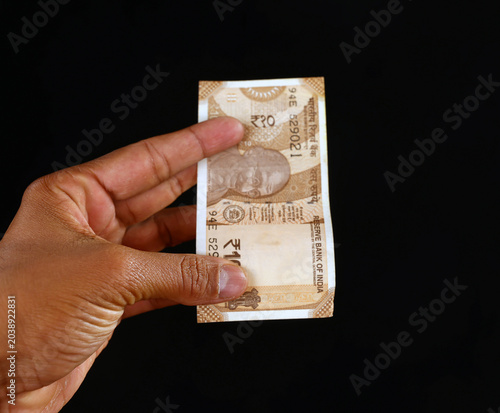 Close-up of a person holding a ten Indian rupee banknote against a solid black background, showcasing currency details and Mahatma Gandhi portrait
