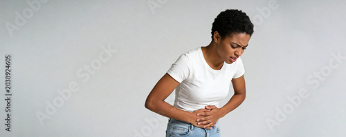 African american woman suffering from severe abdominal pain. Girl clutching stomach due to gastroenteritis or food poisoning. Concept of health problem, medical illness and discomfort.