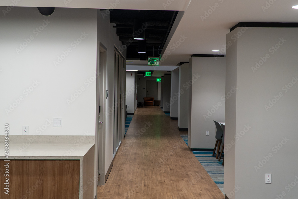 Naklejka premium Modern Office Building Hallway Interior with Contemporary Design, Wooden Floor, and Illuminated Exit Signs, Emphasizing Clean Architecture and Commercial Space Aesthetics