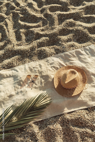 Straw hat, sunglasses, towel, on beach sand background. Aesthetic lifestyle, summer vacation concept. Sunbathing, beach party, picnic on summer holiday. Travel fashionable blog, social media.