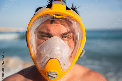 Caucasian man wears full face snorkeling mask near the sea with close portrait view during sunny summer beach vacation. Snorkeling and underwater recreation