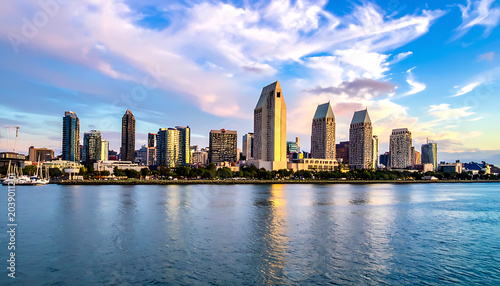 City skyline at sunset over the water, modern skyscrapers reflecting golden light with dramatic clouds in the sky, urban landscape