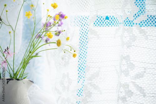 Delicate wildflowers in a vintage pitcher against a lacy white curtain