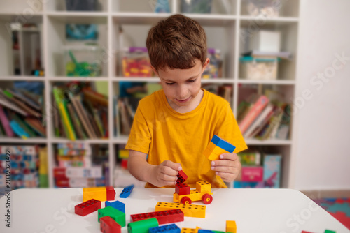 Smiling boy sorting colorful toy blocks on table, smiling child engaged in creative building activity, smiling preschooler playing with constructor in kindergarten room