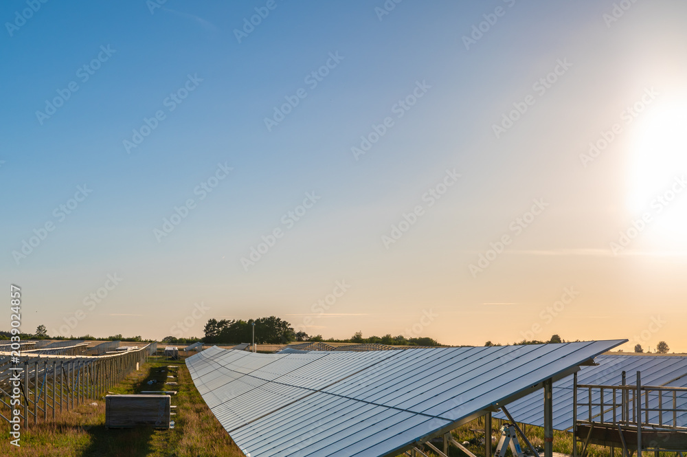 Naklejka premium Solar panel farm at sunset with copy space, renewable energy concept Wide panoramic view of a solar power plant at sunset with long rows of photovoltaic panels and large copy space, ideal for energy 