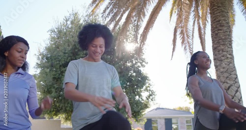 African American friends gathering under palm tree, warming up by doing in-sync knee lifts on deck