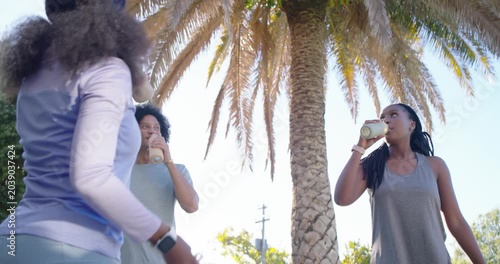 African American friends reacting to legs entering by palm tree, greeting, sipping reusable bottles