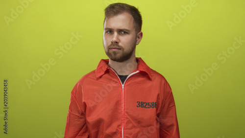 Bild auf Leinwand Man prisoner with beard wearing orange jumpsuit stamped 382586 standing in lime studio with neutral expression, eyes closed; quiet reflection solitude