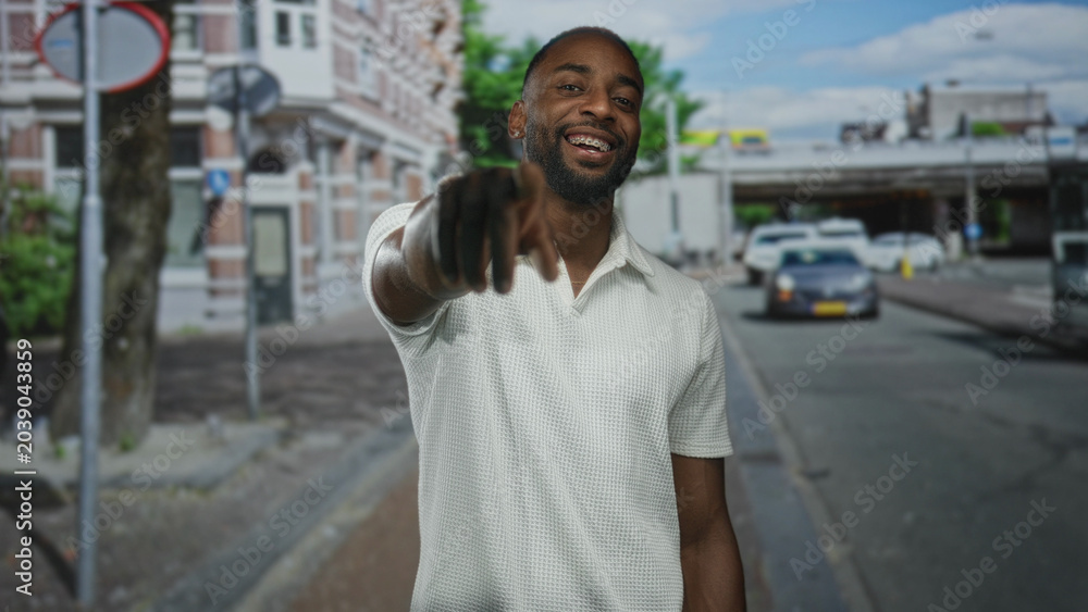 Obraz premium Man points finger and smiles on street wearing white polo and leather glove showing braces and forearm; confidence invitation.