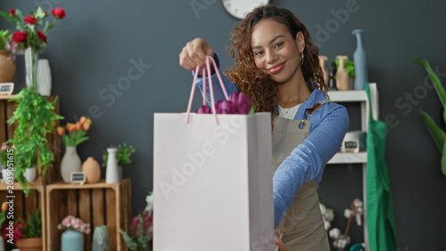 Fotografía Woman florist handing shopping bag with tulips, hand extended offering in a flower studio; joy welcome community
