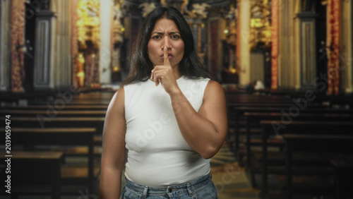Tableau sur toile Woman finger to lips for silence in a building nave with pews and ornate altar; quiet reflection solemnity