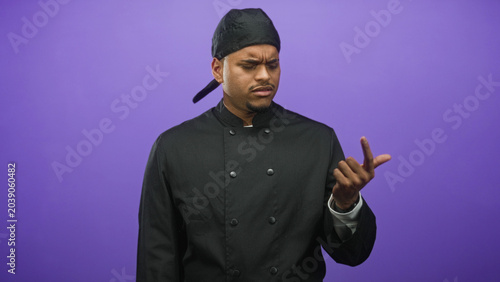 Tableau sur toile Hispanic man chef with beard in black chef uniform and skullcap inspects fingers closely in studio; confusion concentration diligence