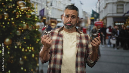 Photography Man holding two faucet valves with bare hands visible on street near decorated christmas tree, pouting expression; plumbing frustration