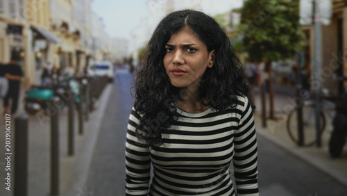 Photography Brunette woman with closed eyes and head tilted back on a busy city street wearing a striped top and visible cheek piercings; quiet contemplation