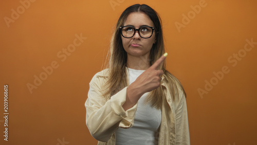 Woman crossing arms and pointing fingers showing yellow nails in studio with orange backdrop; defiance.