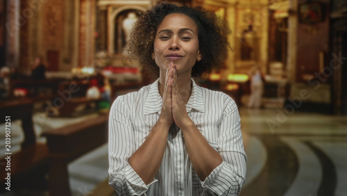 Bild auf Leinwand Woman praying with hands clasped inside a church building, eyes closed and head tilted upward in worship; devotion