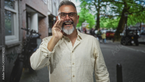 Fotografie Man cupping hand to mouth calling loudly on a city street with trees and buildings behind him; joy celebration community voice