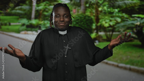 Photos Man priest shrugs arms with cross necklace on street, hands open in casual shrug; playful bemusement