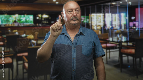 Cuadro en lienzo Man points finger at camera in a restaurant building, raising index finger in a clear pointing gesture; assertive warning