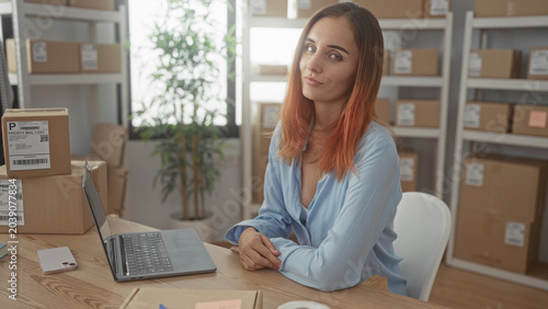 Foto Redhead woman typing on laptop with hands on keyboard amid stacked shipping boxes in a building; entrepreneurial focus