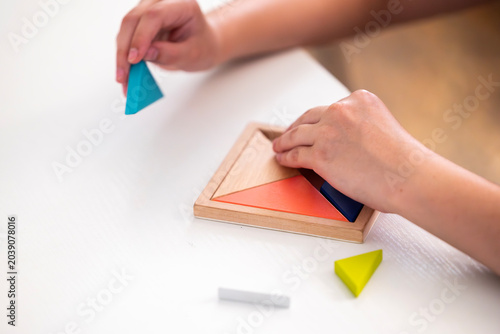 Foto Hands of a child arrange colorful triangular wooden pieces into a square frame d
