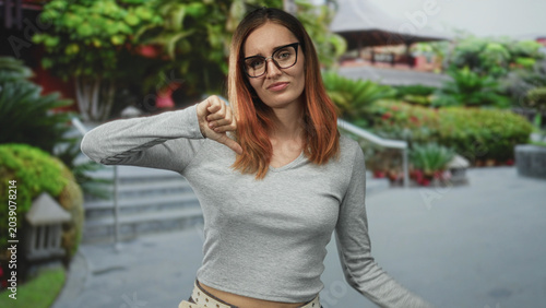 Foto Woman with glasses showing thumbs down gesture on a street with steps and greenery; disapproval rejection