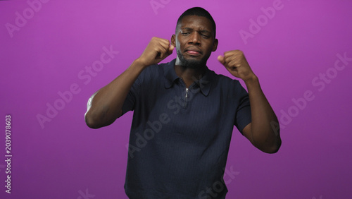 Canvas Print Man raising fists and pouting with closed eyes in studio against a purple backdrop, wearing a polo shirt; playful groove