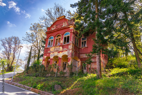 Bild auf Leinwand Weathered Red Abandoned House Among Tall Trees
