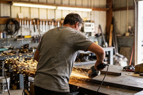 A man in a workshop works with a grinder on metal.
