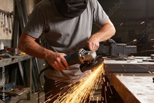 A man in a workshop works with a grinder on metal.