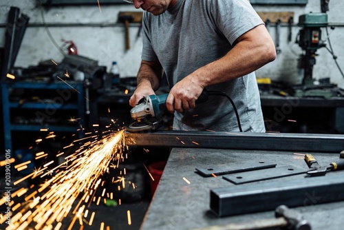 A man in a workshop works with a grinder on metal.