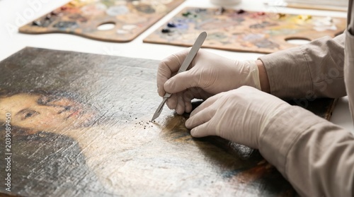 Art conservator carefully removing dirt from an old oil painting with a scalpel