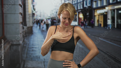 Photography Woman pinches nose with fist near face, sports bra and bare midriff on street with tram visible; disgust