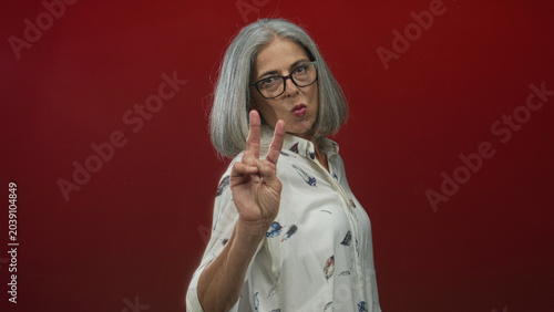 Konstfotografi Woman showing peace sign with hand and puckered lips in a red studio; playful confidence self expression