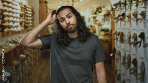 Fotografía Man scratching head with hand in a store building aisle lined with shoes on shelves, looking puzzled; confusion indecision