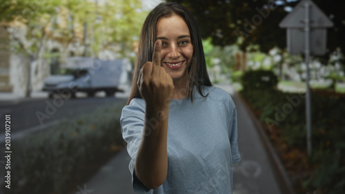 Bild auf Leinwand Young hispanic woman shows middle finger on city street in daylight, standing near bike lane and parked van; defiance