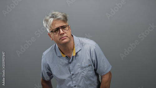 Fotografie Middle aged man with glasses tilts head and squints, hands on hips in a studio; pensive quiet reflection