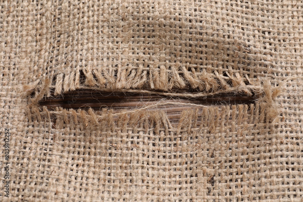 Obraz premium Burlap fabric with torn hole on wooden table, top view