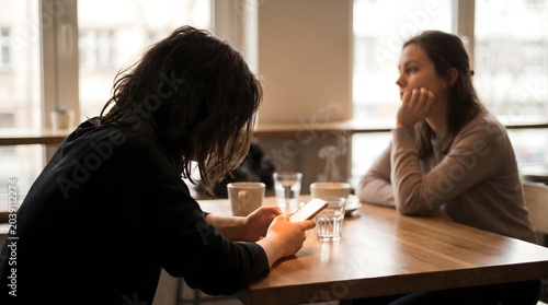 Disconnected friends at cafe woman scrolling on smartphone while other person looks lonely and ignored over coffee