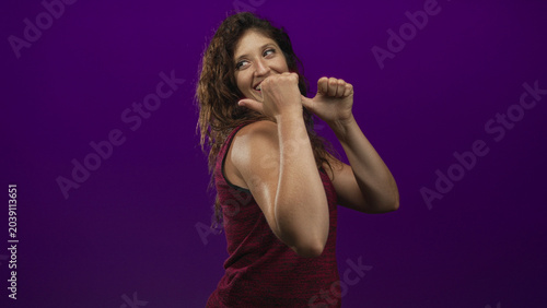 Slika na platnu Young hispanic woman with thumbs to chest wearing a sleeveless tanktop in a purple studio; playful confidence
