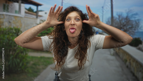 Photography Woman with arms crossed and hands visible on a seaside street promenade near a stone wall and shrubs; playful confidence