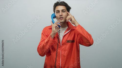 Tableau sur toile Man prisoner in orange jumpsuit holds blue handset to ear and points finger to cheek in studio; isolation reflection