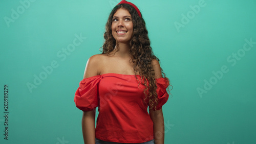 Tableau sur toile Hispanic woman with bare shoulders smiling with eyes closed and head tilted in a turquoise studio wearing a red off shoulder blouse; youthful joy