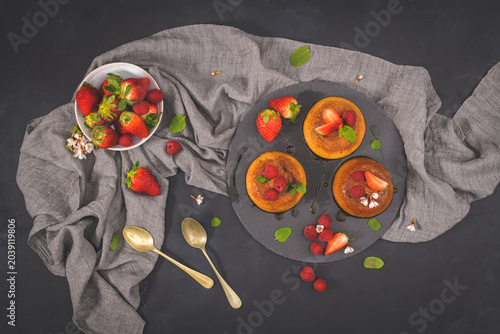 Photos This flat lay food photography captures three golden pancakes garnished with fresh strawberries, raspberries, and mint leaves