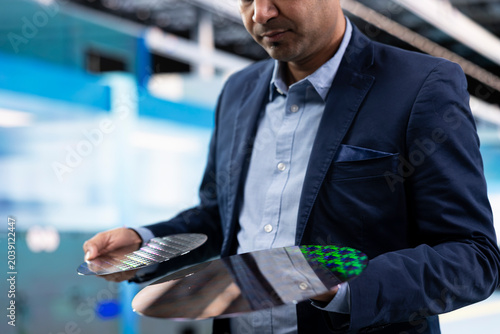 Foto Comparing silicon wafers, semiconductors and Indian man inside high tech manufacturing plant, Innovating microelectronics technology, microchip substrate and management executive in factory